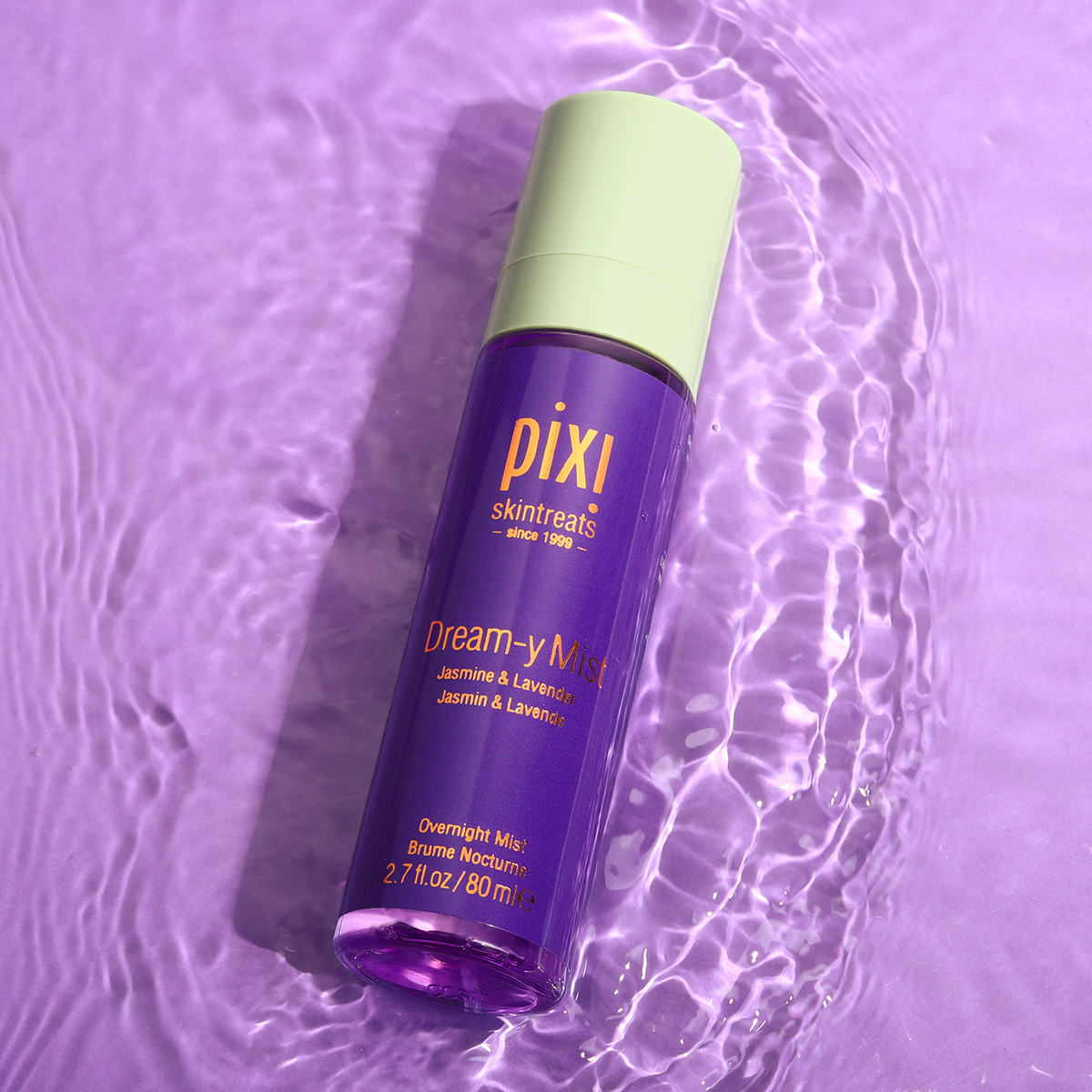 A bottle of PIXI Dream-y Mist sleep-enhancing elixir on a purple background with water ripples around it, indicating movement and freshness.