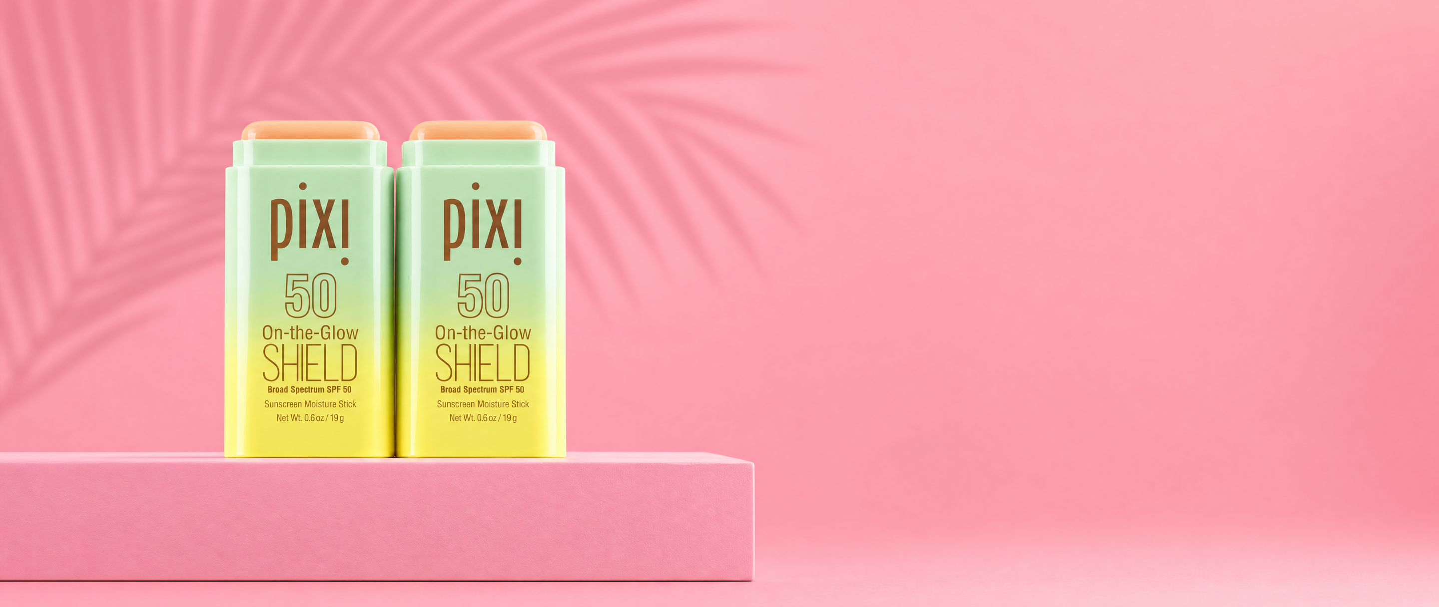 Two Pixi On-the-Glow Shield SPF 50 bottles on a pink background with a shadow of a plant - View 2