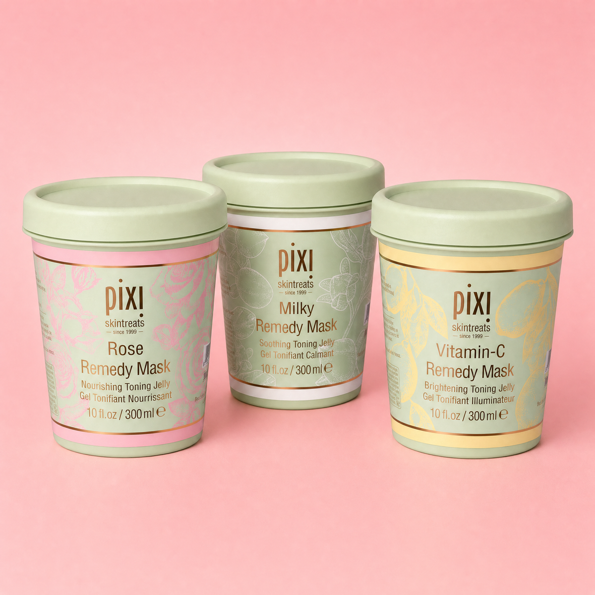 Three Pixi skincare mask jars arranged in a triangle on a solid pink background. The left jar is Rose Remedy Mask with a pink label and mint lid; the center jar is Milky Remedy Mask with a pale green label and mint lid; the right jar is Vitamin-C Remedy Mask with a yellow label and mint lid.