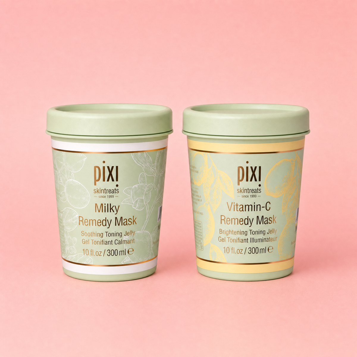 Two Pixi Remedy Masks on a solid pink background. The left tin is for 'Milky Remedy Mask' in a light sage green color, and the right tin is for 'Vitamin-C Remedy Mask' in a pale yellow-green color.