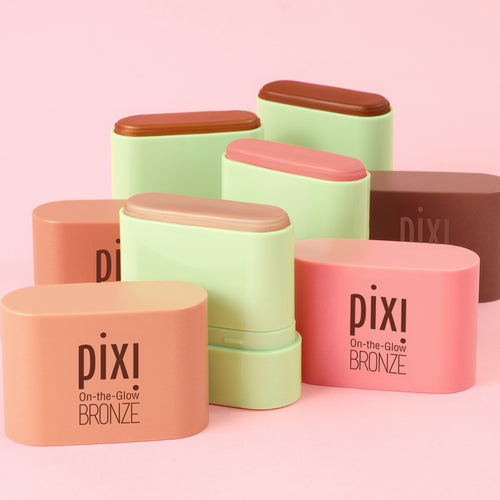 Six Pixi On-the-Glow Bronze stick blush compact cases in various shades of peach, pink, and light green, arranged on a solid pink background. view 1