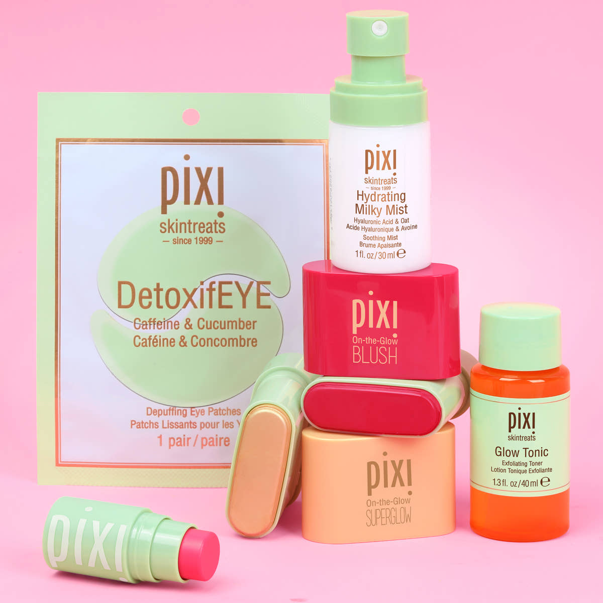 Pixi Skintreats skincare set on a pink background, featuring DetoxifEYE eye patches, a Hydrating Milky Mist, a Blush, a Superglow, and a Glow Tonic in pastel green, coral, peach, and orange packaging.