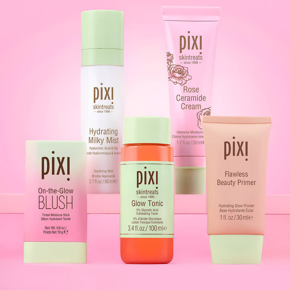 Six Pixi skincare and cosmetic products arranged together on a pink background. The products include Pixi Flawless Beauty Primer, Pixi On-the-Glow Blush, Pixi Glow Tonic, Pixi Hydrating Milky Mist, Pixi Rose Ceramide Cream. On a pink background. view 1