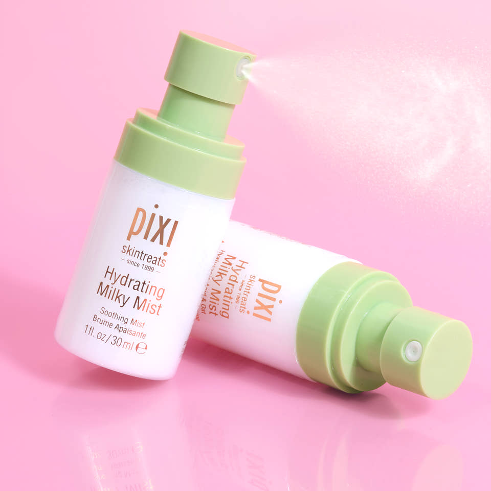 Pixi Skintreats Hydrating Milky Mist Petites bottle shown upright and lying on its side on a pink reflective surface, with mist visible from the pump. view 2
