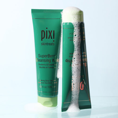 Two Pixi Skintreats SuperBerry Cleansing Whip skincare tubes on a light blue background, one upright showing the SuperBerry Cleansing White product and the other leaning with white lathering foam covering part of the tube. view 2
