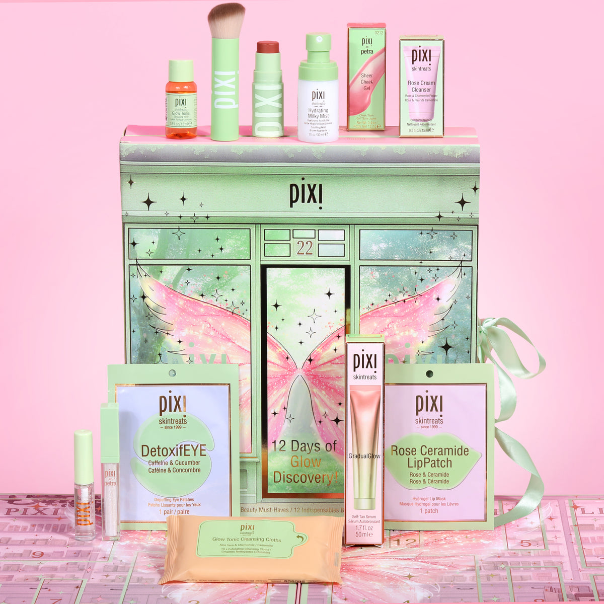 Pixi Beauty 12 Days of Beauty Discovery Advent Calenadr arranged on a pink background, featuring a pastel green gift box with wing artwork, assorted skincare and makeup items, and a pink ribbon.