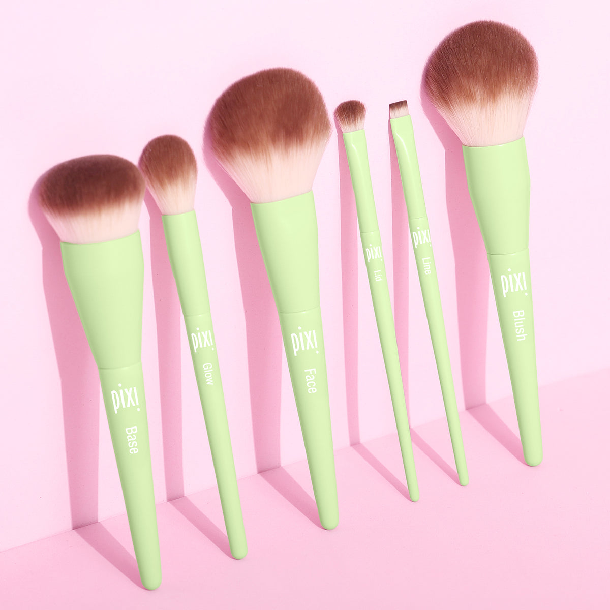 Set of Pixi makeup brushes with green handles on a pink background
