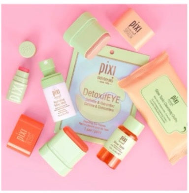 A flat-lay arrangement of Pixi Petites products on a solid pink background, including DetoxiEYE, On-the-Glow Blush and SuperGlow Petites and others.