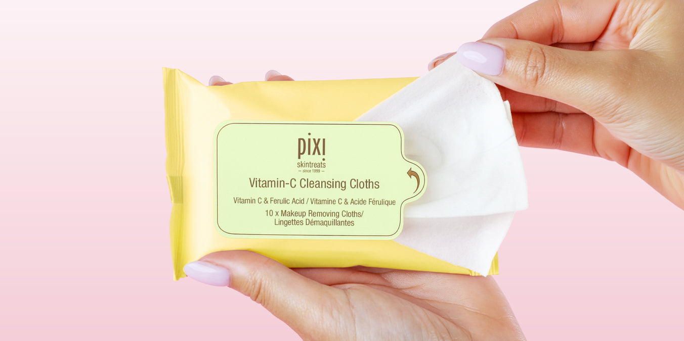 Vitamin-C Cleansing Cloths on a pink background being opened with a hand