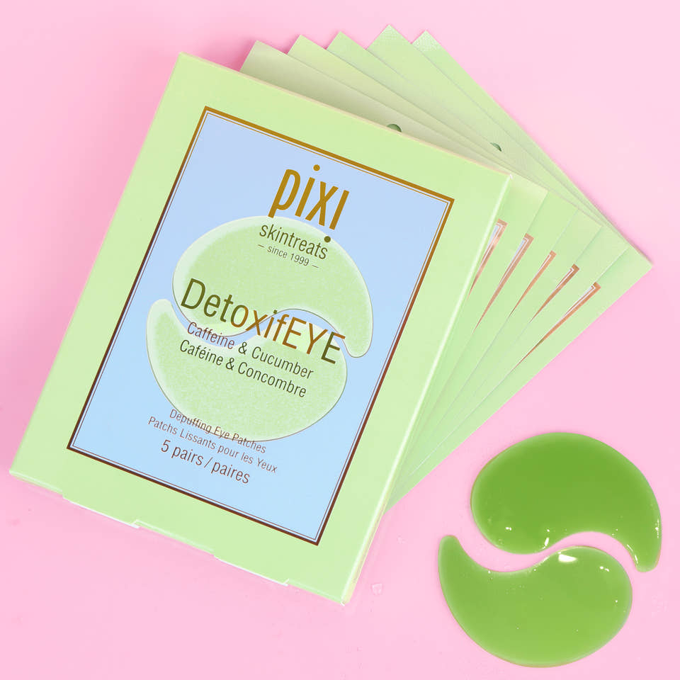 A stack of Pixi Skintreats DetoxiEYE eye gel patches in a light green box, displayed on a pink background with two green gel patches placed in front. view 1