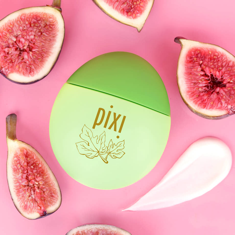 Pixi HandHero PixiFig scented hand lotion surrounded by fresh figs, including a swatch to show texture on a pink background. view 2