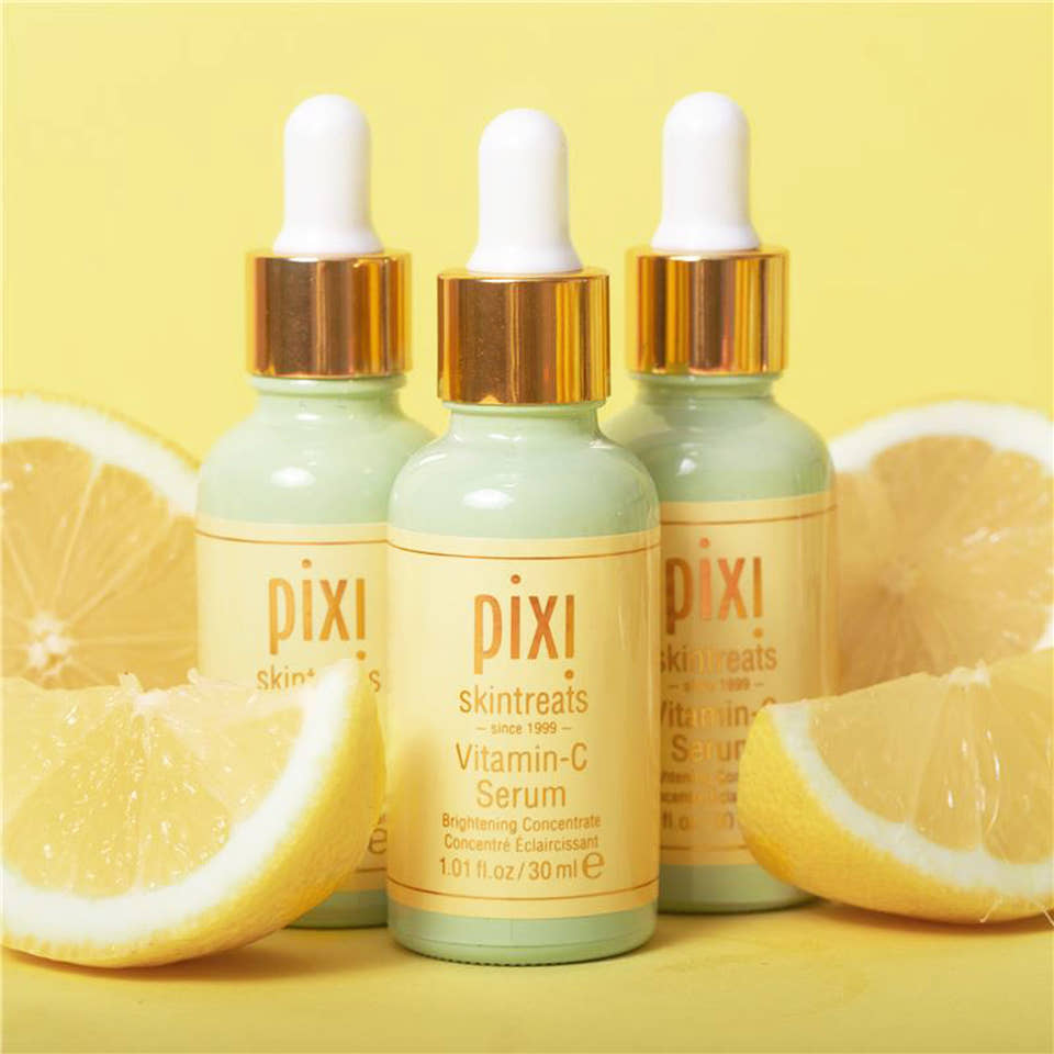 Three bottles of PIXI Vitamin-C Serum with dropper caps, positioned against a yellow background with sliced lemons on each side. view 1