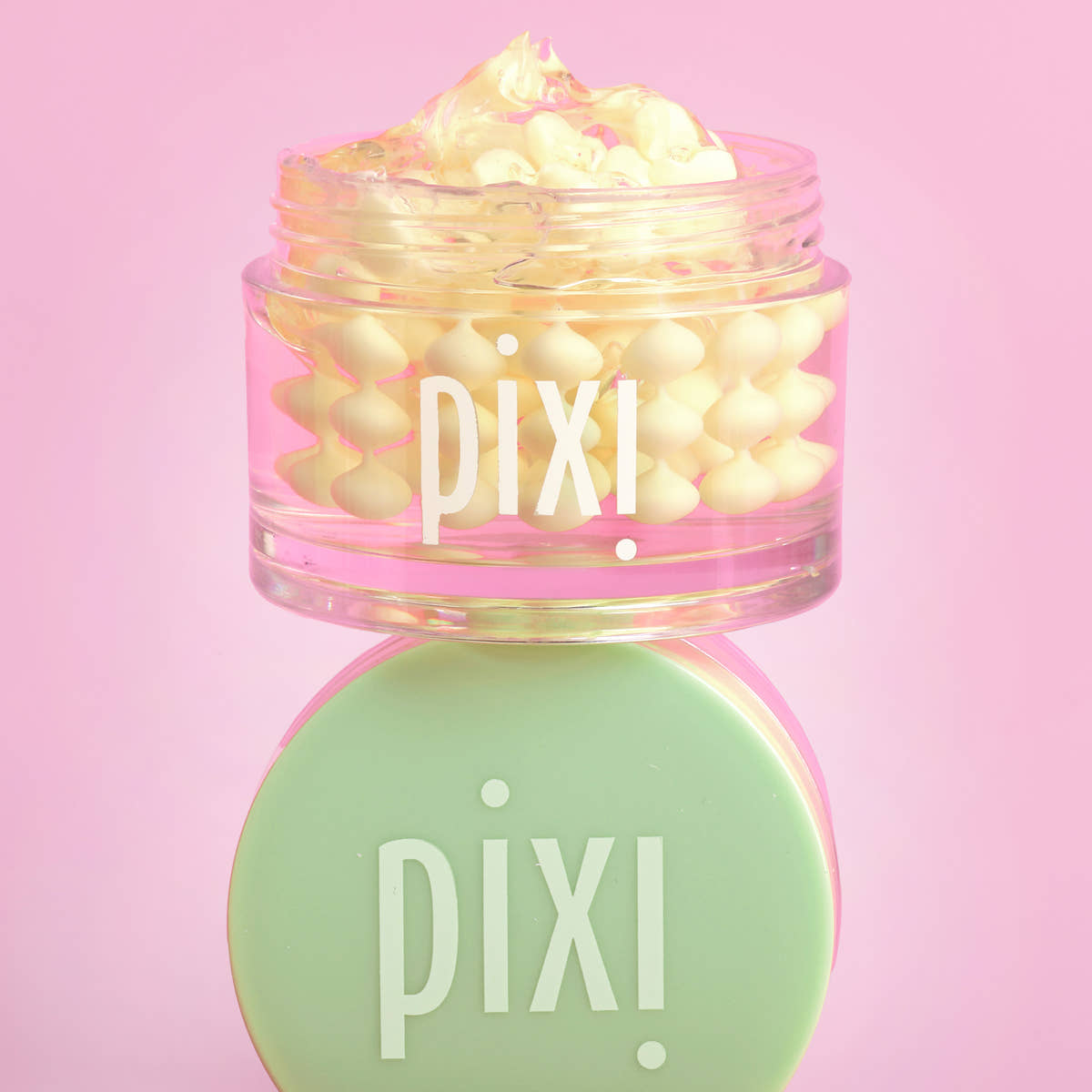 Pixi Vitamin-C CremeSerum in a clear jar with a mint green lid, set against a solid pink background.
