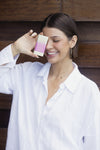 Woman holding a skincare product against her face with a wooden background